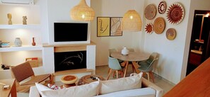 A living room with a fireplace, a television, a dining table with chairs, and various wall decorations.