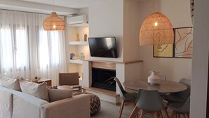 A modern living room with a sofa, dining table, chairs, a fireplace, and a TV. - Europa,2br,2bth Villa With Private Pool And Stunning Sea Views (Skiathos)