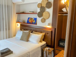 Habitación de hotel con cama, cabecera, mesita de noche, lámpara, estante con libros y un cuadro, y una pared decorada con platos.