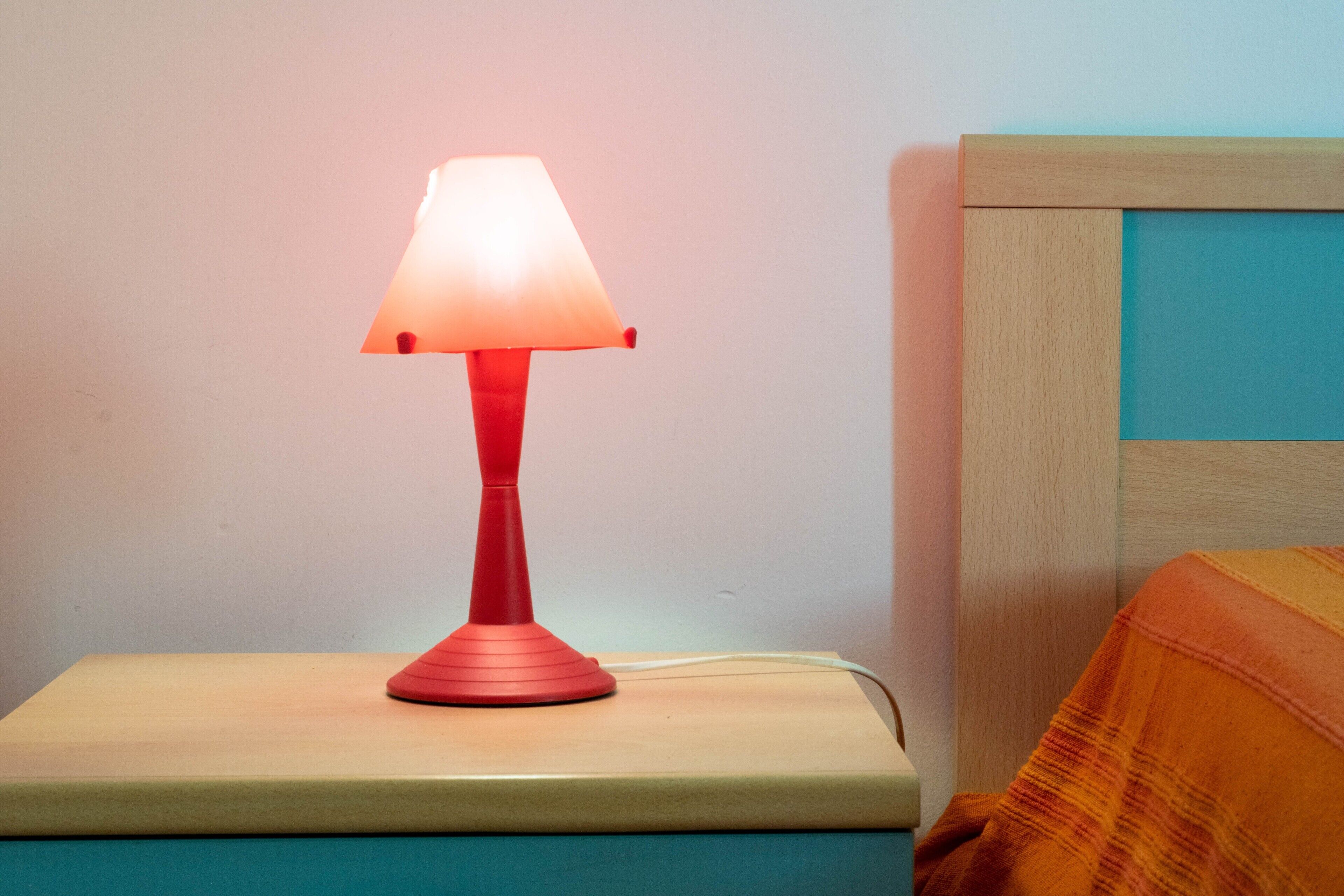 Une lampe de chevet rouge est posée sur une table de nuit, à côté d’un lit doté d’une tête de lit en bois.