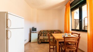 Una habitación compacta con kitchenette, una mesa de comedor con sillas, un sofá y un televisor sobre un mueble bajo.