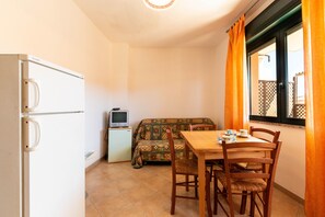 A compact room with a kitchenette, a dining table with chairs, a sofa, and a television on a small cabinet.