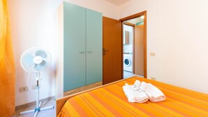 Habitación de hotel con cama, ventilador, armario y lavadora al fondo.