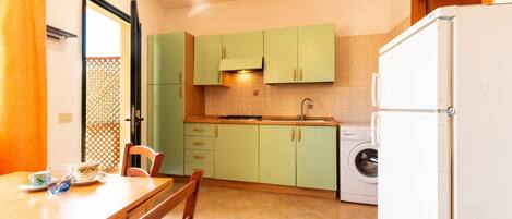 A compact kitchen with a washing machine, a dining table with chairs, and a refrigerator.