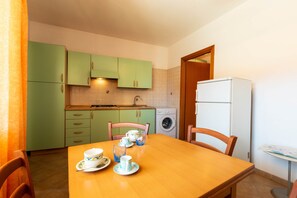 Une cuisine de taille réduite avec des meubles de couleur verte, une table à manger en bois et un lave-linge.