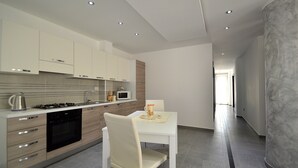 A modern kitchen with built-in appliances, a dining area with a white table and chair, and a hallway with a marble column. - Villa "White" with Private Pool, Terrace & Wi-Fi (Alcamo)