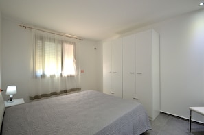 A bedroom with a bed, a nightstand, a lamp, a wardrobe, and a window with curtains.