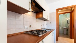 A kitchen with a gas stove, white cabinets, and a view into the bathroom. - City apartment with balcony – Apartment Cavour Codice F (Villasimius)