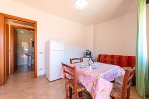 Un coin repas avec une table dressée pour deux personnes, un réfrigérateur et un banc.