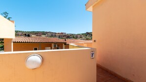A balcony with a view of a residential area, a door with a 'F' sign, and a window with a circular view. - City apartment with balcony – Apartment Cavour Codice F (Villasimius)