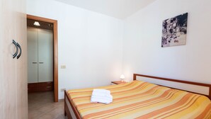 A hotel room with a bed, a nightstand, a wall-mounted lamp, a door leading to a bathroom, and a painting on the wall. - City apartment with balcony – Apartment Cavour Codice F (Villasimius)