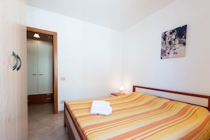 A hotel room with a bed, a nightstand, a wall-mounted lamp, a door leading to a bathroom, and a painting on the wall.