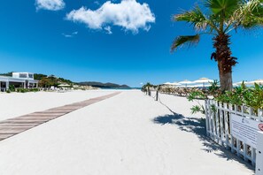 A beach pathway leading to a sandy beach with umbrellas and palm trees. - City apartment with balcony – Apartment Cavour Codice F (Villasimius)