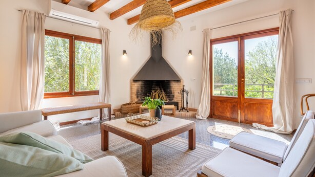 A cozy living room with a fireplace, wooden beams, large windows, and comfortable seating. - Holiday Home "Sa Teulera de Sencelles" with Pool & Wi-Fi (Sencelles)