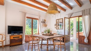 A spacious room with a wooden dining table, chairs, a television, and a large window with curtains. - Holiday Home "Sa Teulera de Sencelles" with Pool & Wi-Fi (Sencelles)