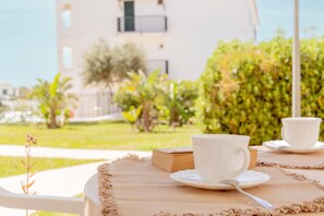 A table with two white cups and saucers, a book, and a woven placemat.