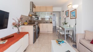 Una cocina moderna con microondas, horno y lavavajillas, un comedor con mesa y sillas, y una sala de estar con sofá y televisión de pantalla plana.