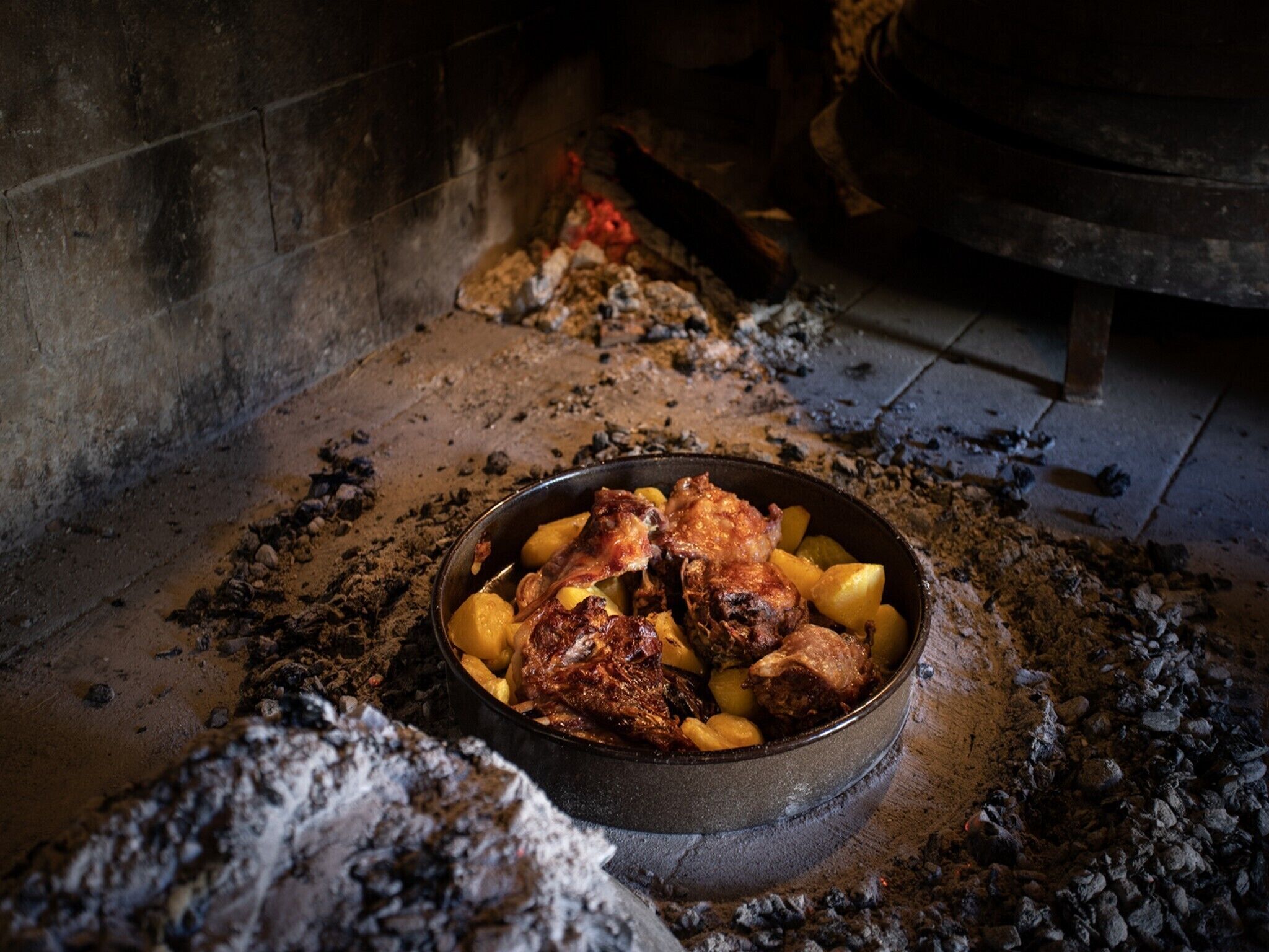 A rustic stone oven with a bowl of roasted meat and potatoes inside.