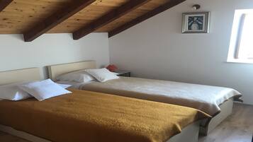 Une chambre avec deux lits simples, des poutres en bois au plafond, un tableau encadré au mur et une fenêtre sur le côté droit.