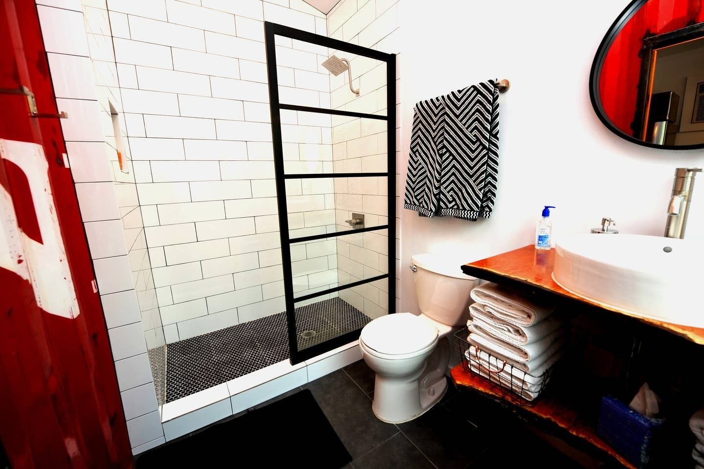 A modern bathroom with a glass shower enclosure, white tiled walls, a white toilet, and a wooden vanity with a mirror.