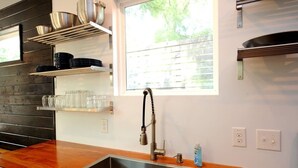 Et moderne køkken med en stålvask, træbordplade og metalkasser med service og glas.