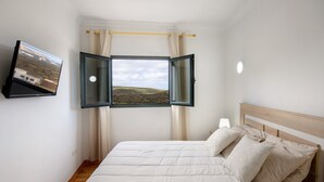 A bedroom with a bed, a window with curtains, a flat-screen TV, and a lamp. - Close to Hiking and Beach with Beautiful Winter Garden - Apartment Ye (Haria)