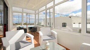 A sunlit patio with white wicker furniture, a glass table, and a view of the sky and buildings. - Close to Hiking and Beach with Beautiful Winter Garden - Apartment Ye (Haria)