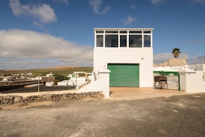 Un bâtiment blanc avec une porte verte, un petit balcon et un mur de pierre à l’avant.