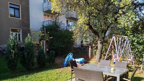 Une terrasse extérieure avec une table et des chaises, entourée de verdure et agrémentée d’une balançoire.