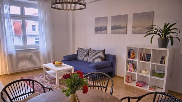 Un salon avec un canapé bleu, une bibliothèque blanche et une table à manger avec des chaises.