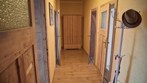 Un couloir en bois, avec des portes de chaque côté, un porte-manteau avec des chapeaux et une armoire en bois au centre.