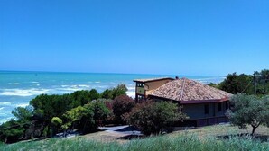 Una casa costera con techo de tejas, rodeada de vegetación y con vista al mar.