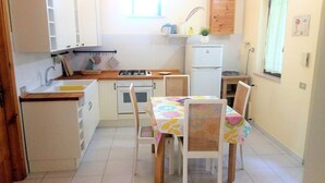 Una cocina compacta con armarios blancos, estufa a gas, lavamanos y un refrigerador pequeño.