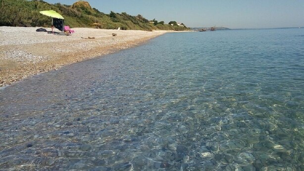 Una playa con aguas poco profundas y cristalinas, una orilla arenosa y algunas sombrillas.