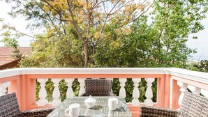 A balcony with wicker furniture and a glass table, surrounded by lush greenery and trees. - Stylish Art Deco Apartment Close To The Beach (Platanias)