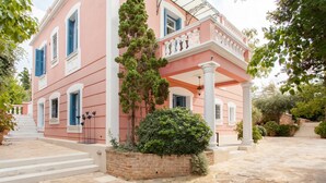 A pink building with white columns and a stone-paved courtyard. - Stylish Art Deco Apartment Close To The Beach (Platanias)