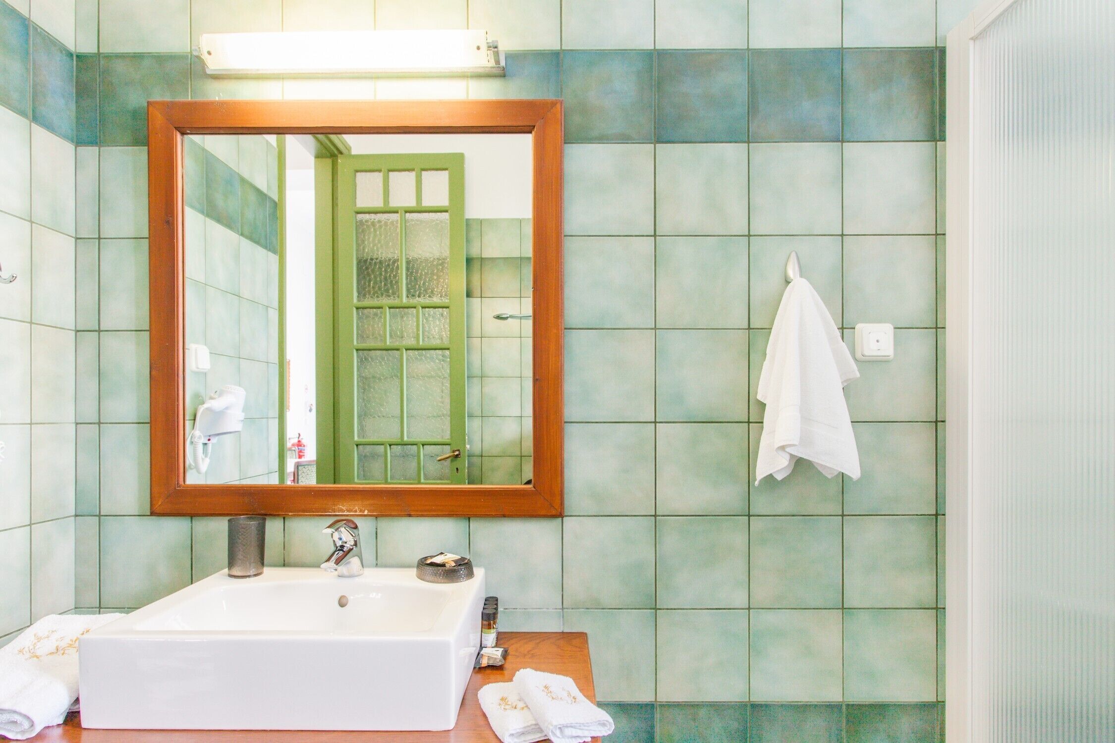 Une salle de bain avec un lavabo rectangulaire, un miroir avec un cadre en bois et une serviette accrochée au mur.