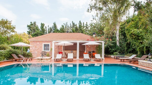 A swimming pool with lounge chairs and umbrellas, surrounded by a brick building and trees. - Stylish Art Deco Apartment Close To The Beach (Platanias)