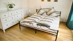 Een keurig opgemaakt slaapkamer met een bed, een dressoir en een klein tafeltje met een lamp.