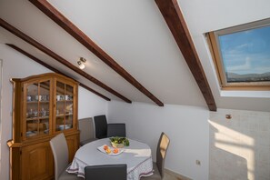 Un espace repas comprenant une table ronde, des chaises, un buffet en bois doté de portes en verre et une vue sur le ciel grâce à une lucarne.