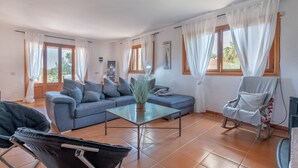 A living room with a sofa, a coffee table, a rocking chair, and a chair with a plant. - Beautiful Country House "Can Cancus" in Nature with Rooftop Terrace, Garden & Wi-Fi (Capdepera)