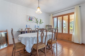 A dining area with a round table, chairs, a chandelier, and a view through a glass door.