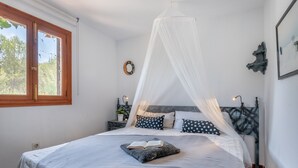 A bedroom with a bed, a window, a bedside table, a nightstand, a wall clock, and a framed picture. - Beautiful Country House "Can Cancus" in Nature with Rooftop Terrace, Garden & Wi-Fi (Capdepera)