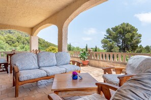 Eine Terrasse im Freien mit einer Holz-Couch, Stühlen, einem Tisch und Kübelpflanzen.
