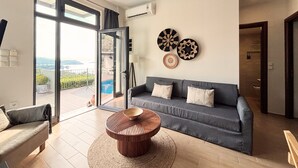 Una sala de estar moderna con un sofá gris, una mesa de centro redonda de madera y vista a una piscina a través de un ventanal.