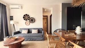 Una sala de estar moderna con un sofá gris, una mesa de comedor de madera y sillas. Se observan adornos en la pared y un equipo de aire acondicionado.