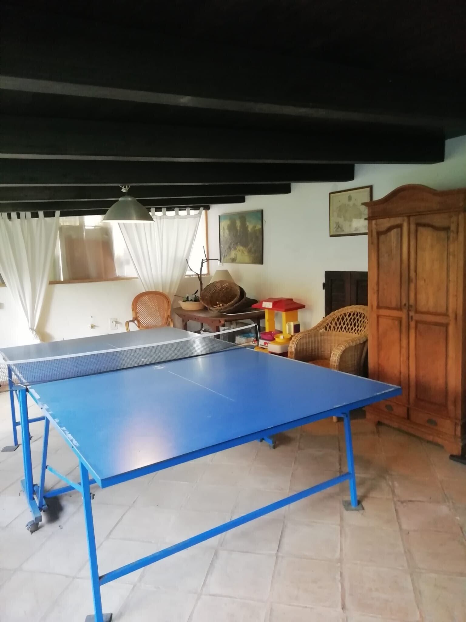 A room with a ping pong table, wicker chairs, a wooden cabinet, and a lamp.