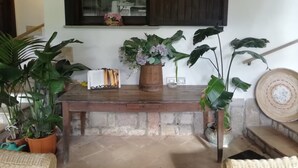 A wooden table with a potted plant, a book, and a wicker chair in a room with a window and a wall-mounted shelf. - Villa Stella Close to the Beach with Wi-Fi, A/C, Garden;Parking (Santa Margherita di Pula)