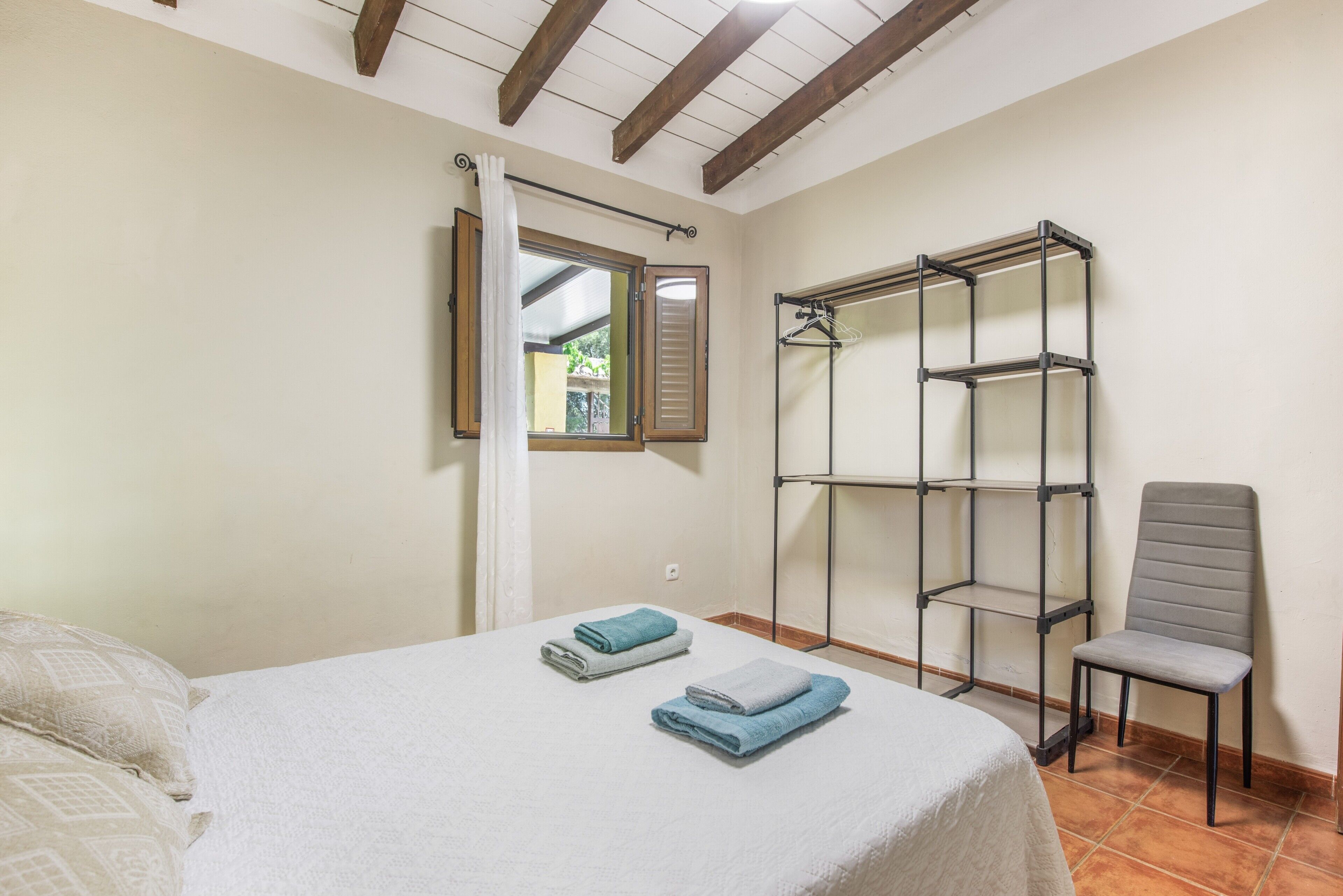 A bedroom with a bed, a chair, a window, and a metal shelf unit.