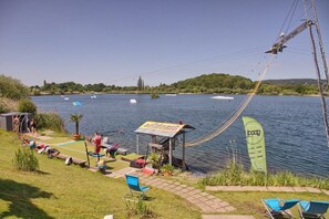 Una zona junto al lago con un pequeño pabellón, sillones de descanso y un teleférico sobre el agua.